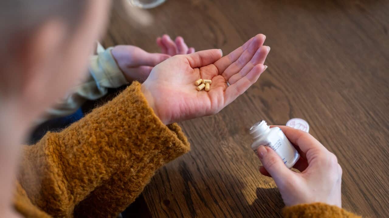 A person in a mustard jumper with pills in one hand and a medication bottle in the other