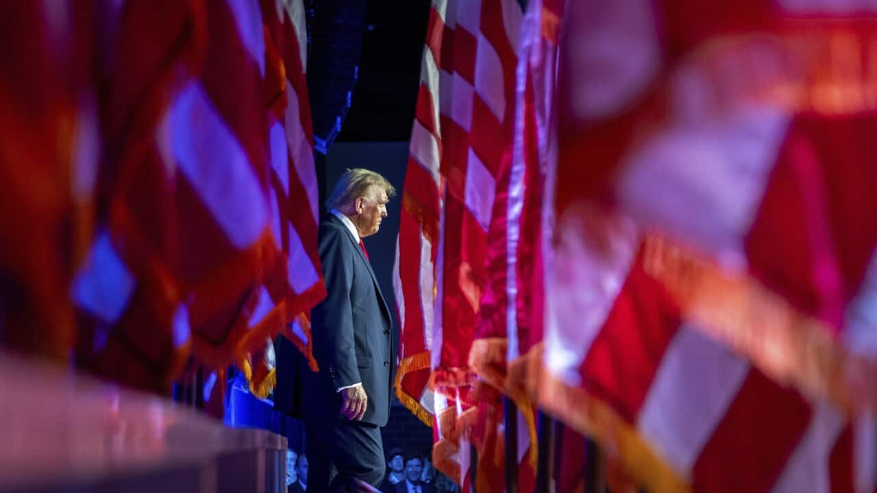 A man wearing a suit walks past a row of flags.