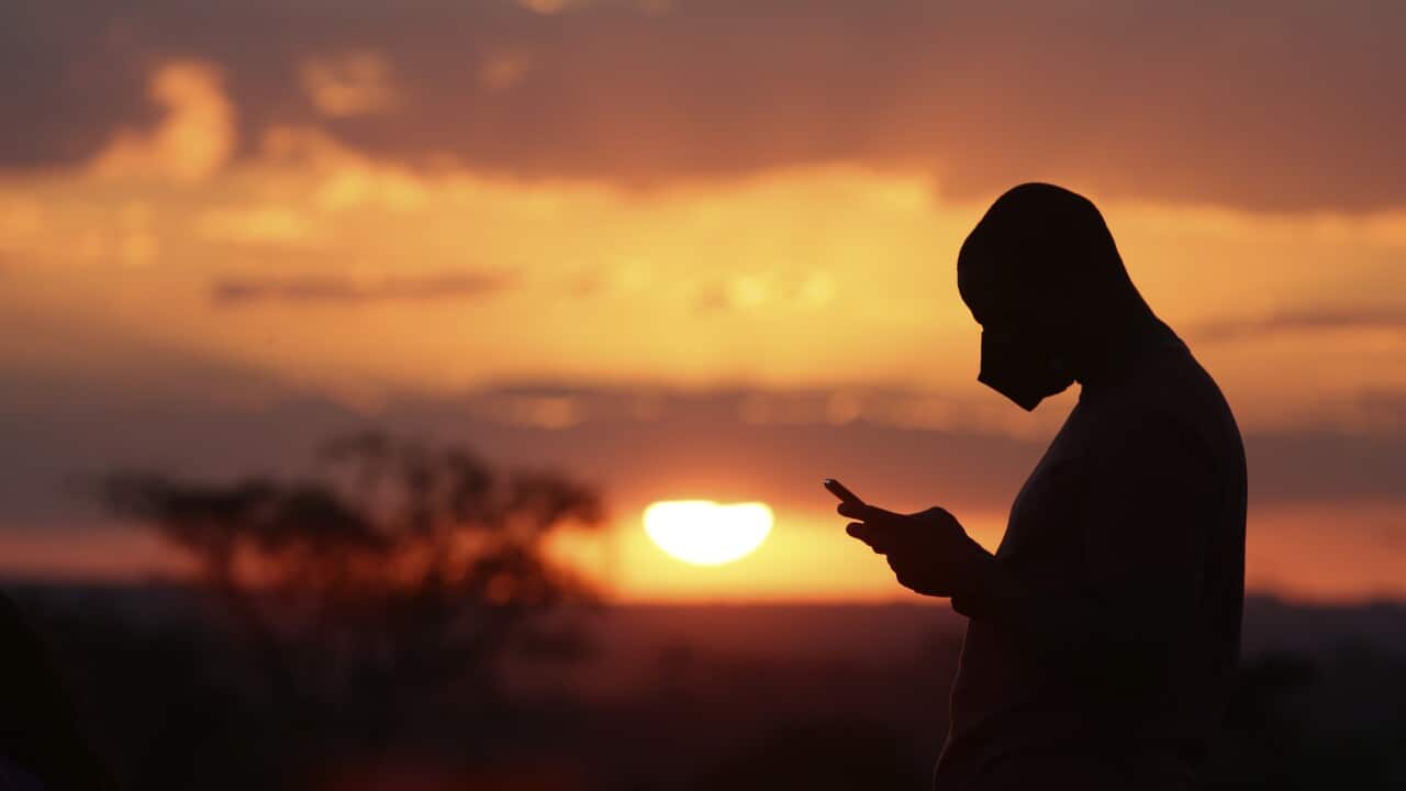 A man wearing a protective face mask is silhouetted against a sunset in the city center after authorities eased the restrictions related to COVID-19, in Brasilia, Brazil, Saturday, July 4, 2020. (AP Photo/Eraldo Peres)