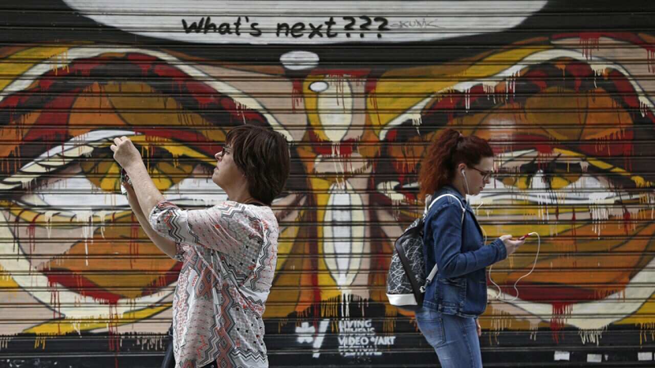 Women walk in front of a closed shop shutter covered with graffiti
