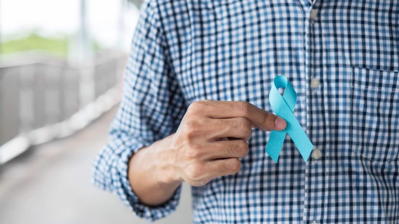 A man holding a blue ribbon for prostate cancer awareness.