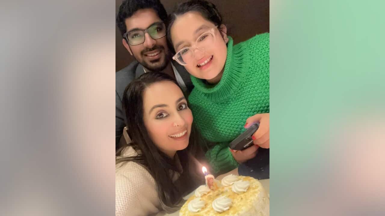 A woman smiles at the camera along with a man and a girl wearing glasses.