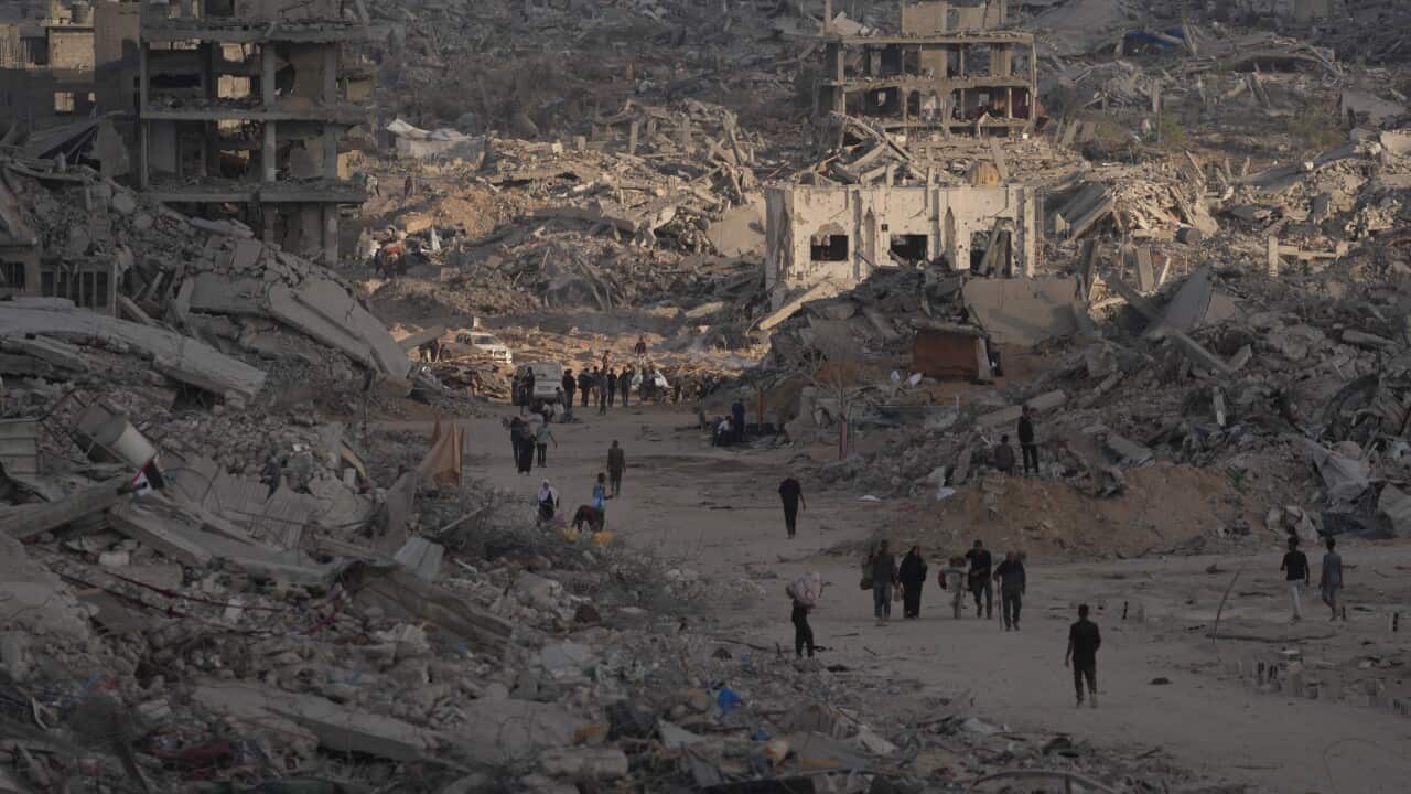 Palestinians walk among destroyed buildings in Gaza City, Sunday, Oct. 12, 2025