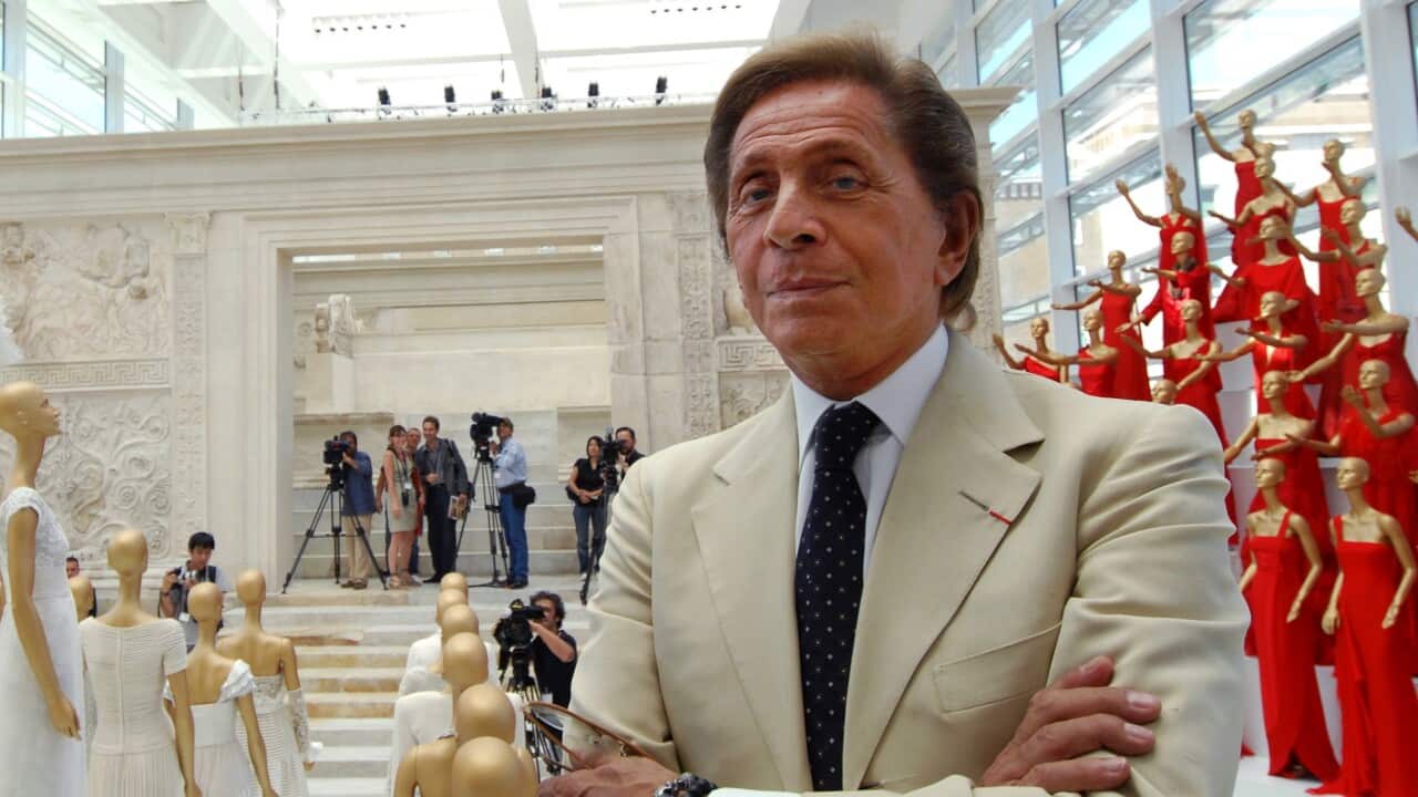 Italian fashion designer Valentino stands with his arms crossd in front of mannequins adorned with his designs
