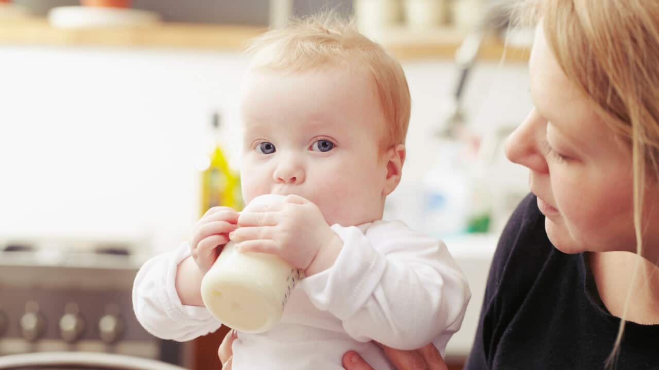 Mother and baby sitting in kitchen with baby bottle