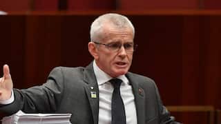 Politician gestures with his hands as he speaks in parliament holding some papers