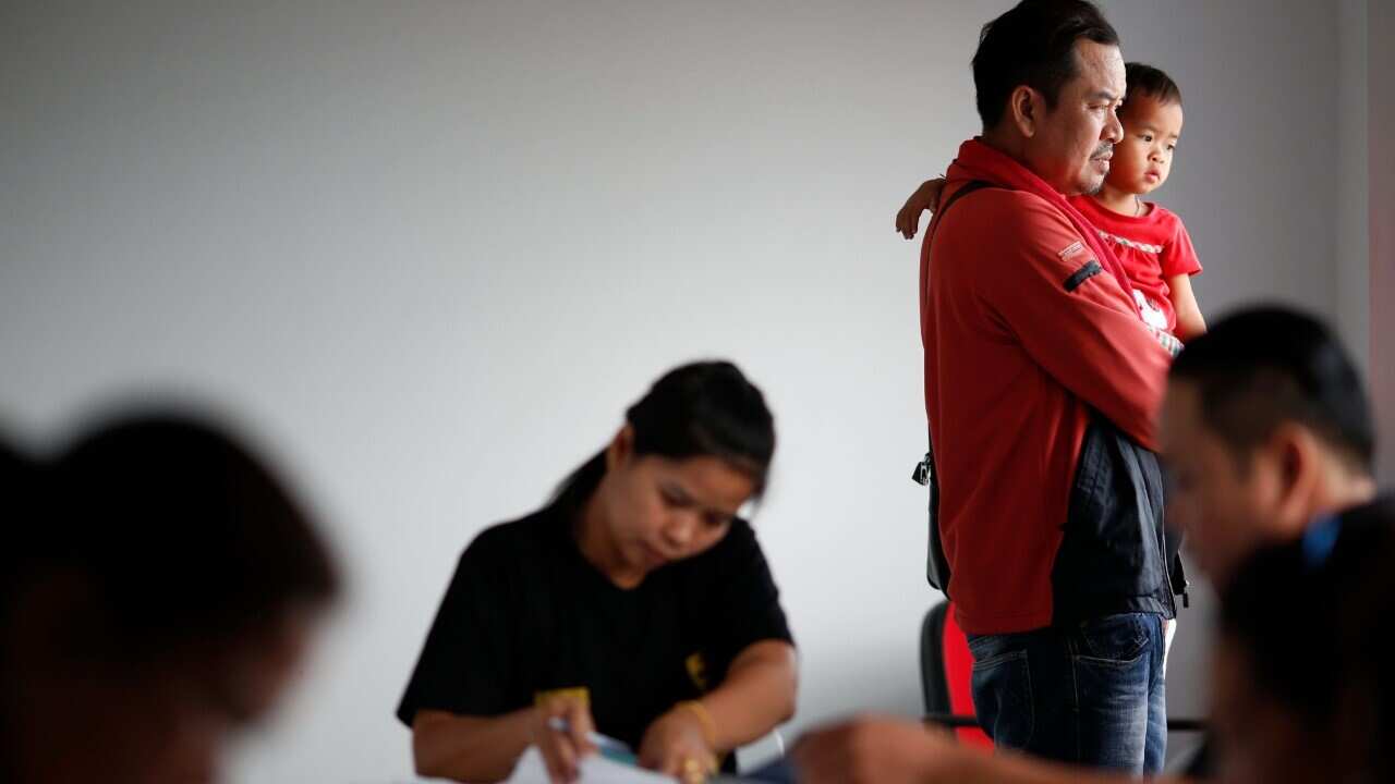 A Lao migrant worker, holds his daughter next to Thai employers during a registration drive at the Employment Office in Samut Sakhon province, Thailand (AAP Image - EPA - RUNGROJ YONGRIT)