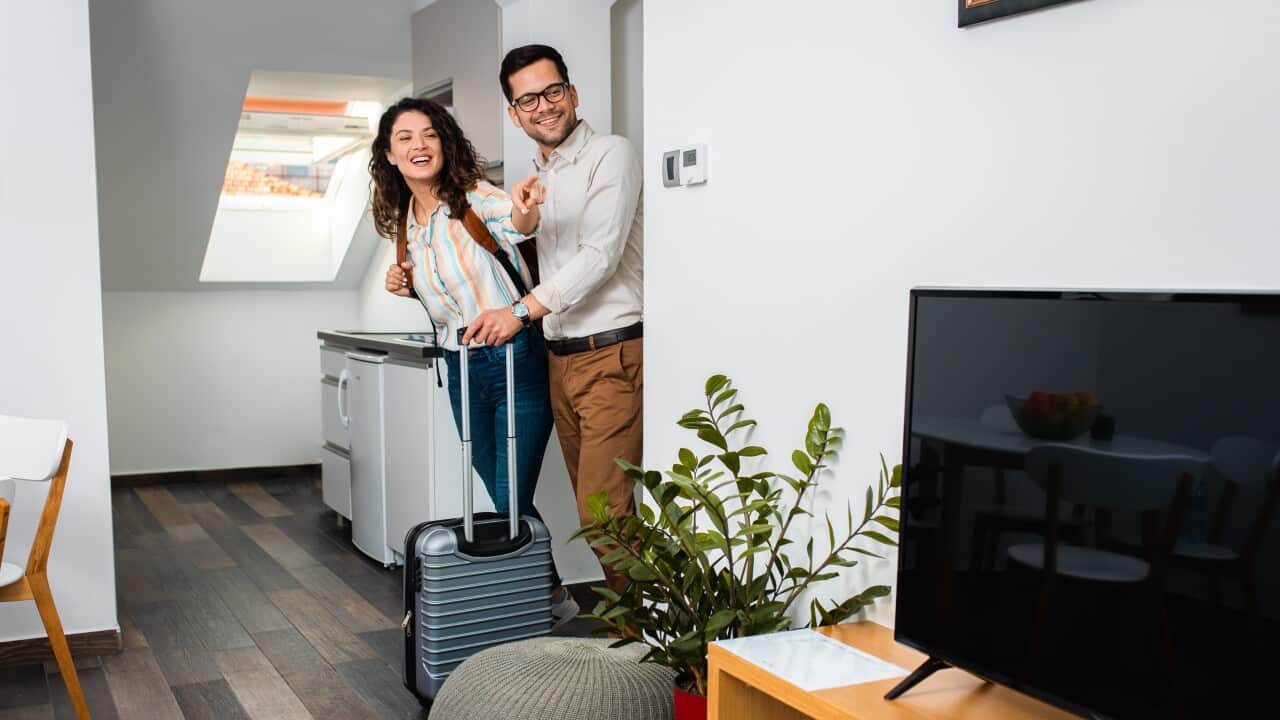 Smiling couple with suitcase arriving in hotel room.