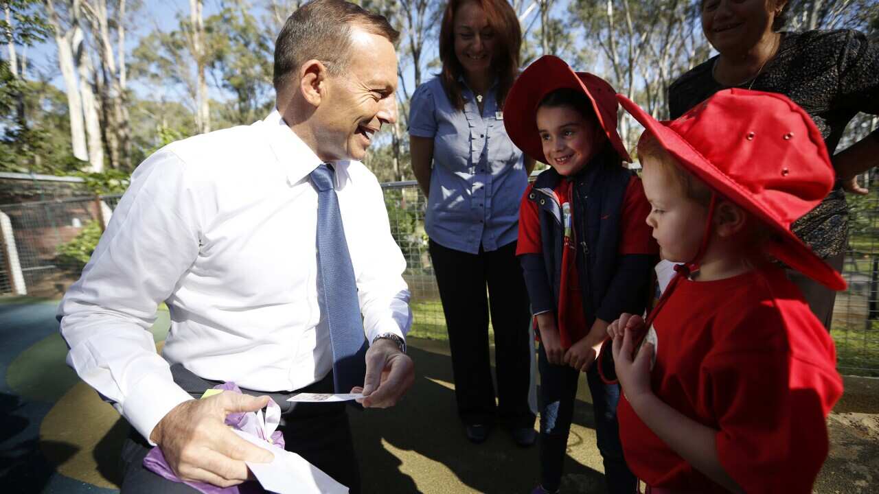 Australian Prime Minister Tony Abbott smiles and laughs as he opens a surprise wrapped present given to him by some children during a visit to a pre-school in Mulgoa, western Sydney, Friday, May 15, 2015. (AAP Image/David Moir) NO ARCHIVING