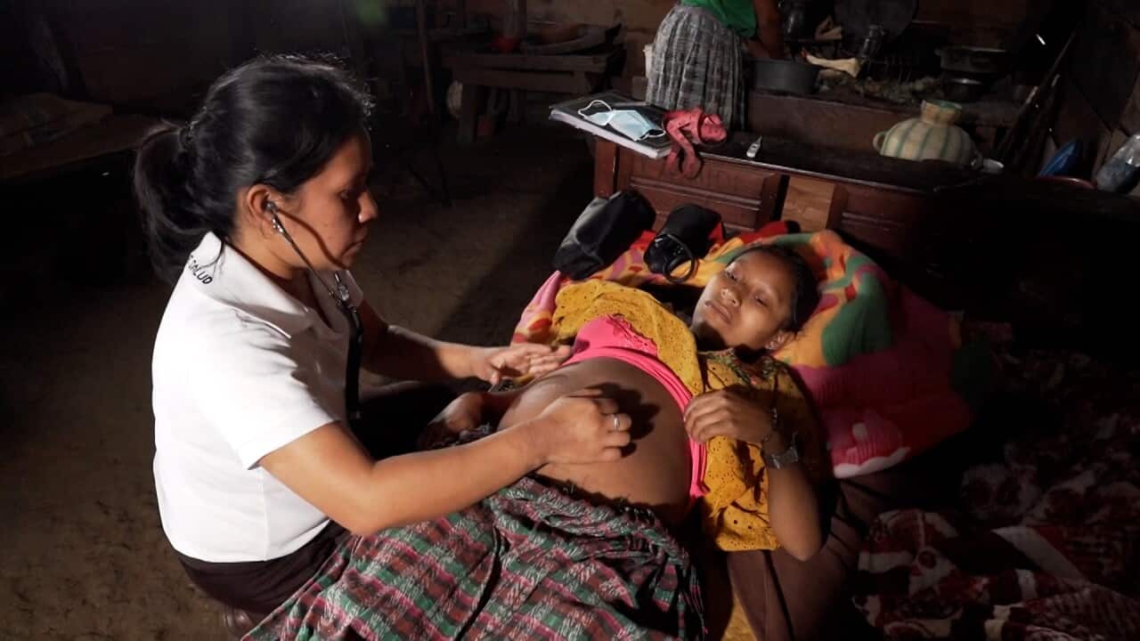 Young pregnant woman lying in a bed and being examined by a female nurse with a stethoscope