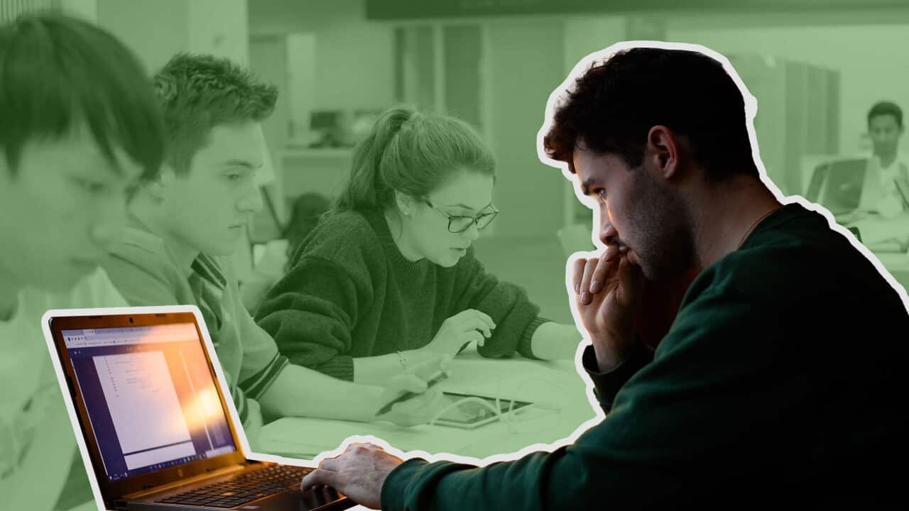 A man navigating his laptop, with one hand on the laptop's mousepad. In the background three other young adults study at their laptops.