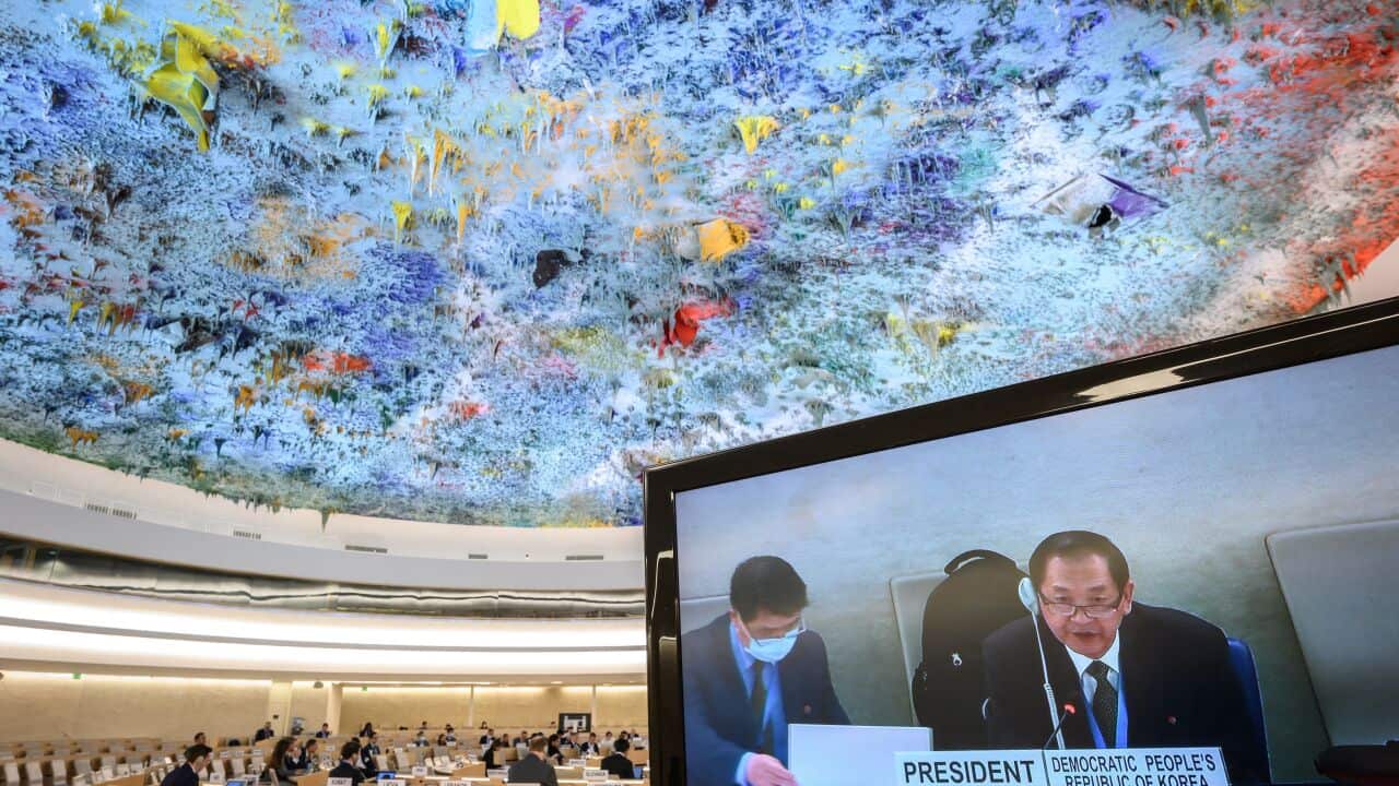A man appearing on a television screen in a large hall