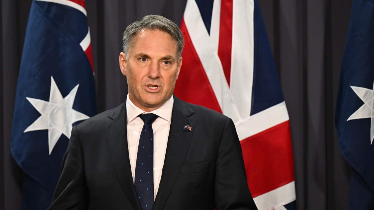 Richard Marles stands in front of an Australian flag giving a press conference.