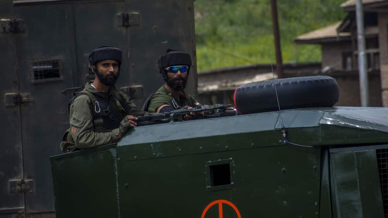 Two soldiers in uniform stand on a military vehicle with arms.