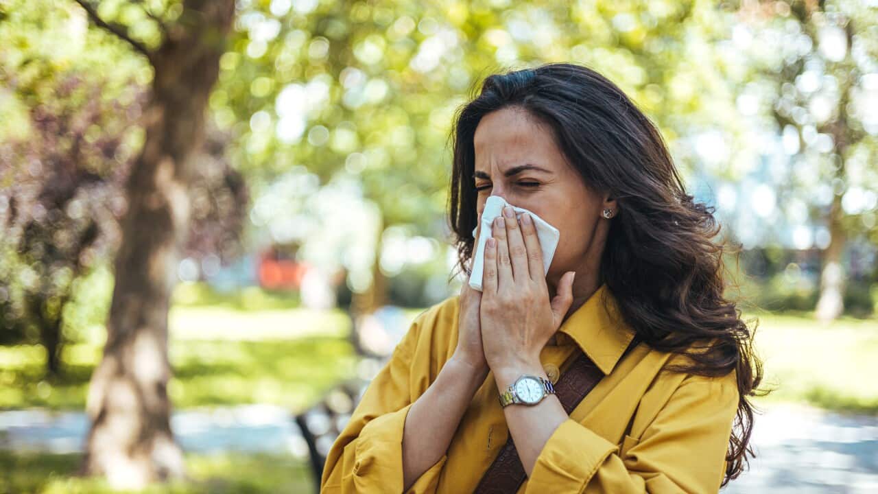A woman standing outside blowing her nose