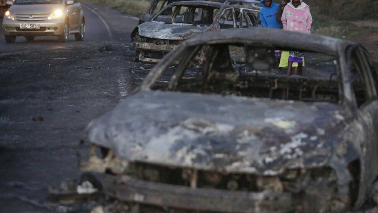 People walk amongst burned down cars