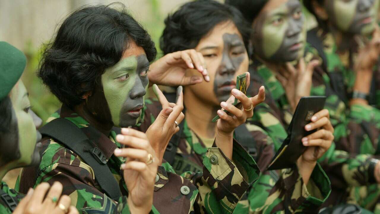 Woman soldiers apply camouflage face paint as they prepare for a parade at a ceremony commemorating the 58th anniversary of the Indonesian Army in Jakarta, Monday, Dec. 22, 2003. (AP Photo/Dita Alangkara)