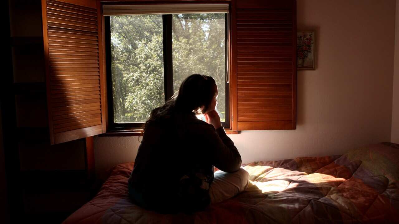 Young woman sitting on a bed facing away from the camera