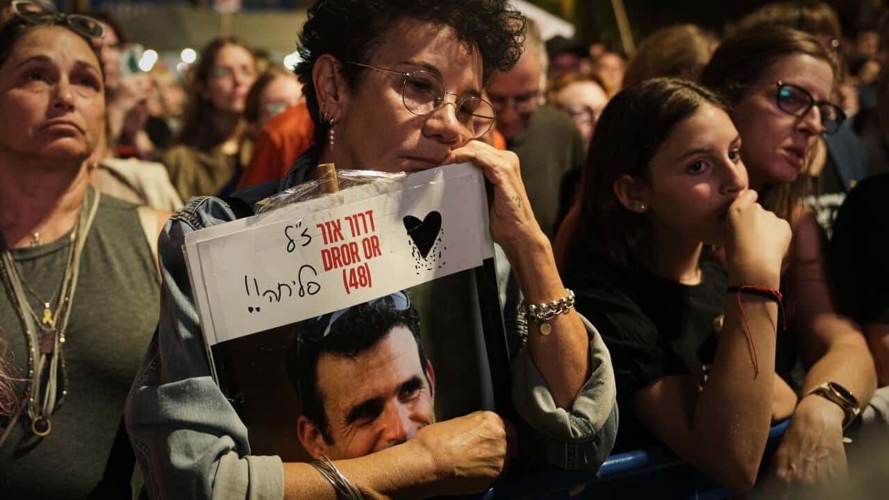 A woman holds a placard in her hands at a rally with other rallygoers around her.