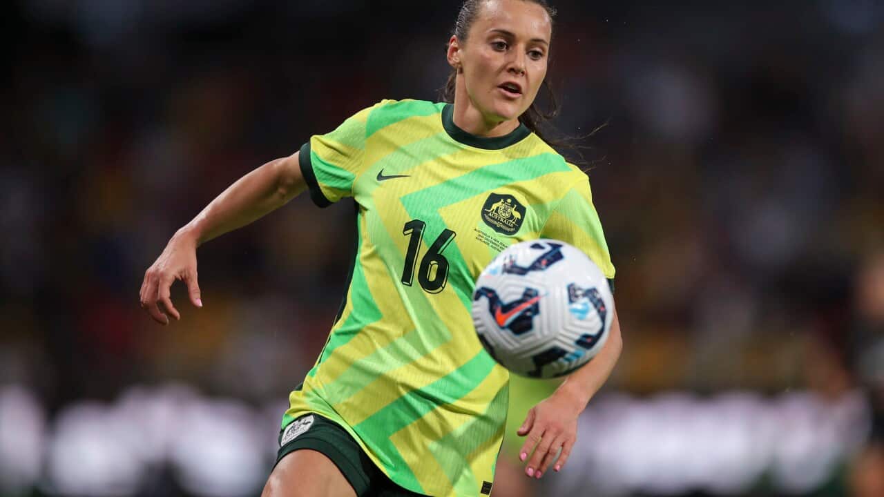 A women in a yellow and green football shirt running behind a football