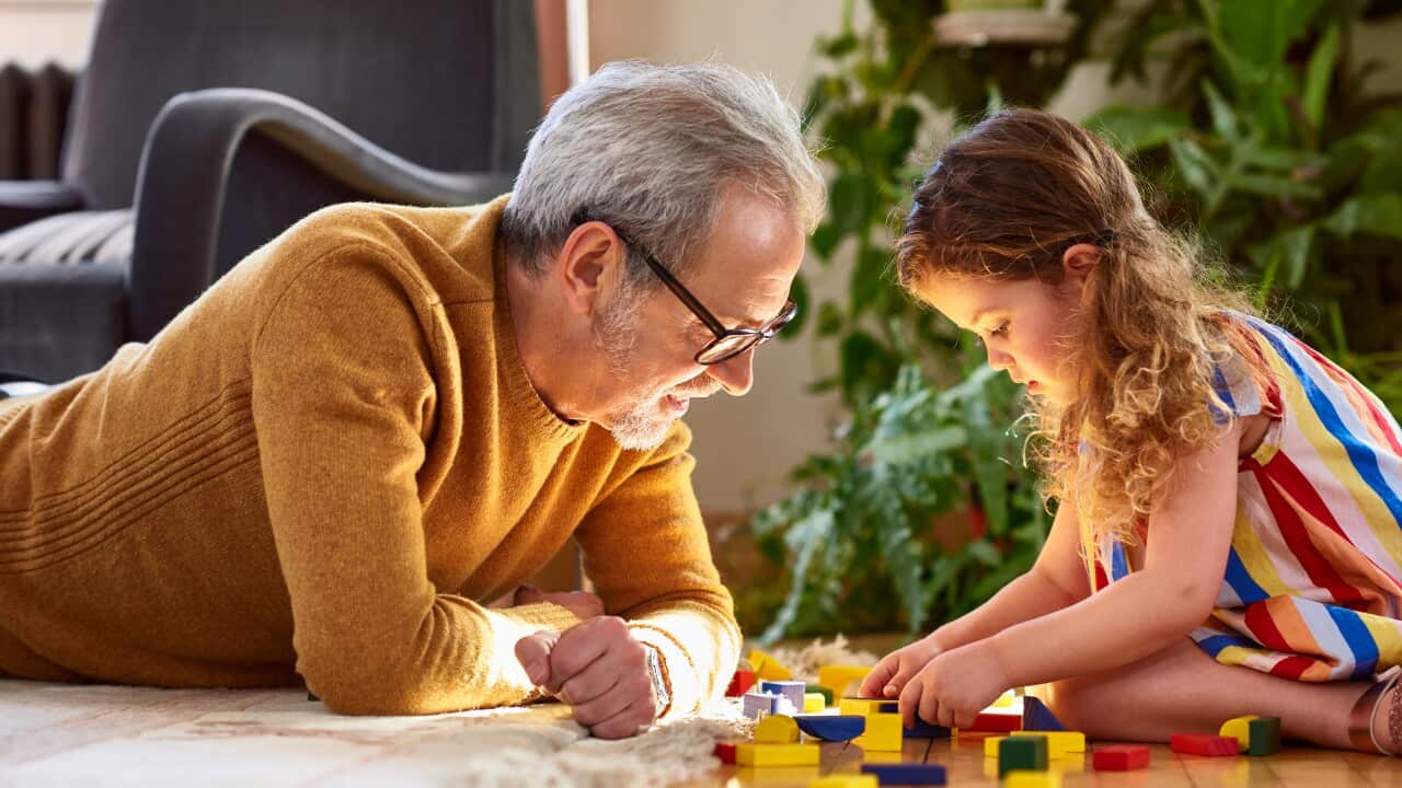 Granddaughter playing with wooden block and granddad watching