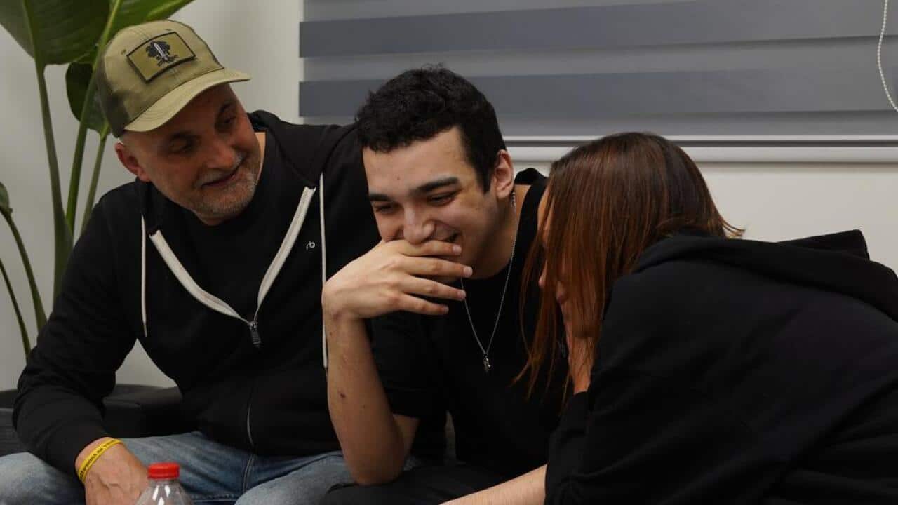 Edan Alexander sits between a man and a woman inside