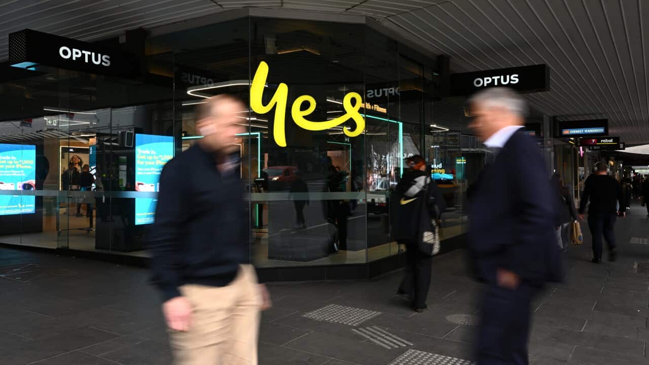 Two blurred figures walk past a store front with a large yellow sign reading 'Yes'