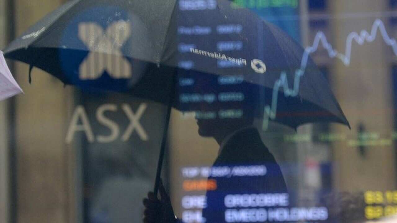 A man with an umbrella is reflected on a window showing the ASX