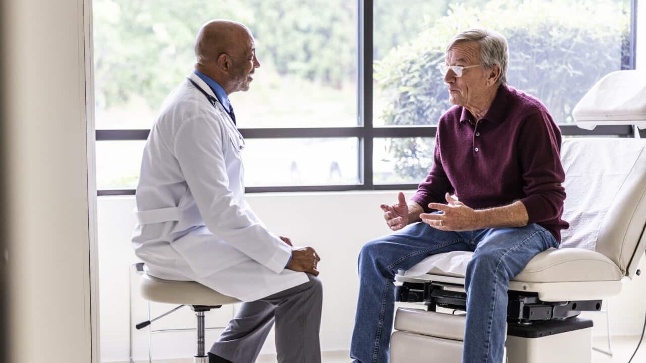 A doctor is speaking with a patient seated in a white recliner chair.