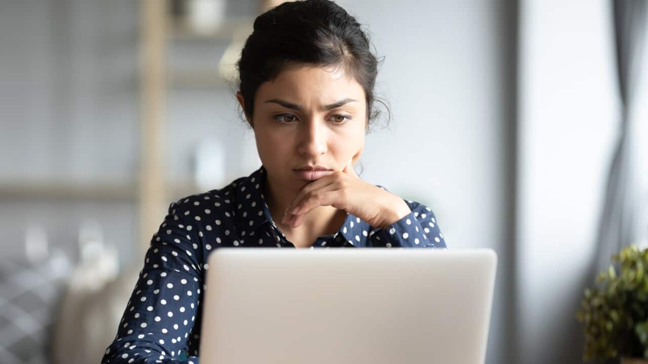 A woman frowning while reading something on her laptop.