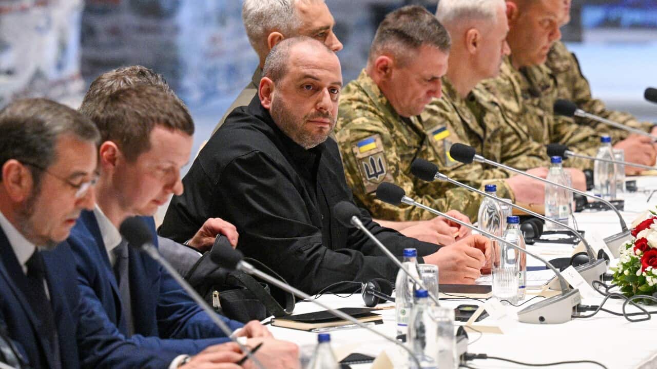 Ukraine's defence minister Rustem Umerov with other members of a delegation, seated at a white table with microphones and bottles of water.