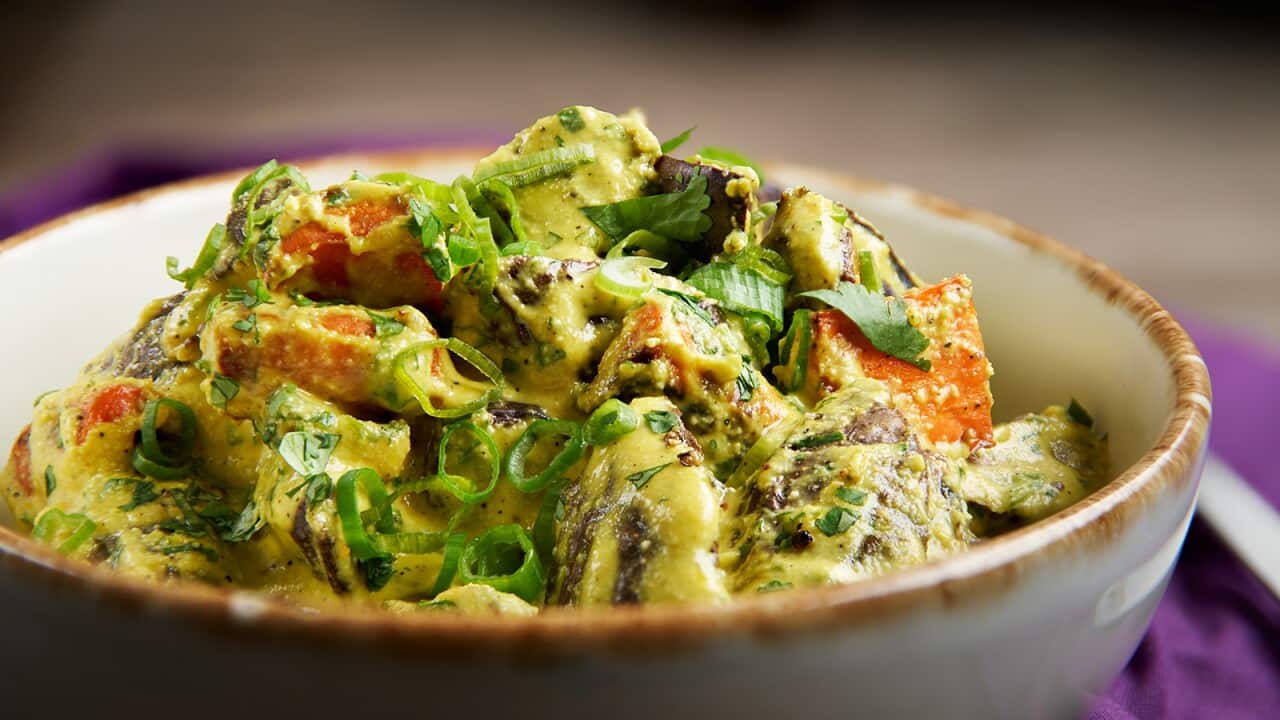 A cream pottery bowl with brown lip is filled with a vibrant salad with a creamy yellowish dressing.