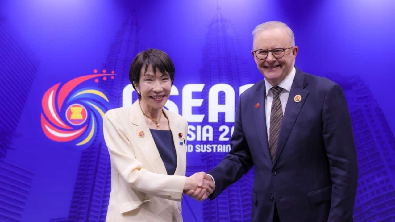 Man and woman shaking hands, smiling at camera in front of blue wall