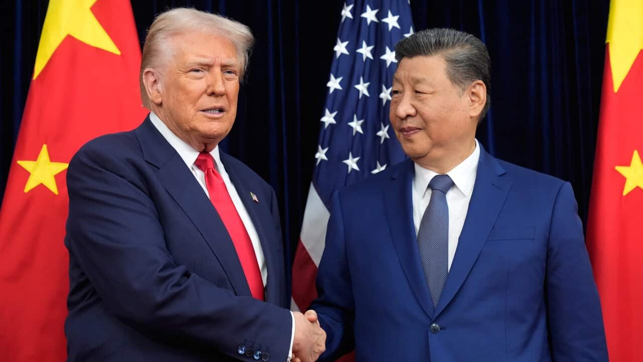 Donald Trump and Xi Jinping, both in suits, hold hands in front of the US and Chinese flags.