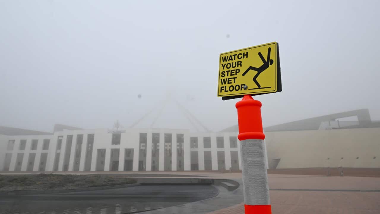 A sign altering to ‘wet floor’ is seen in front of Parliament House shrouded in fog in Canberra.