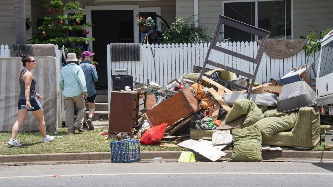 Three people walk into a house with damaged furniture on the front lawn.