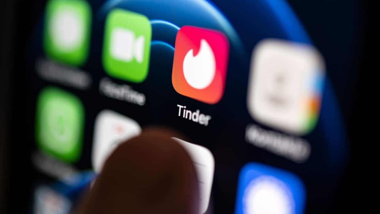 A person using a smartphone hovering his finger over the Tinder app icon.