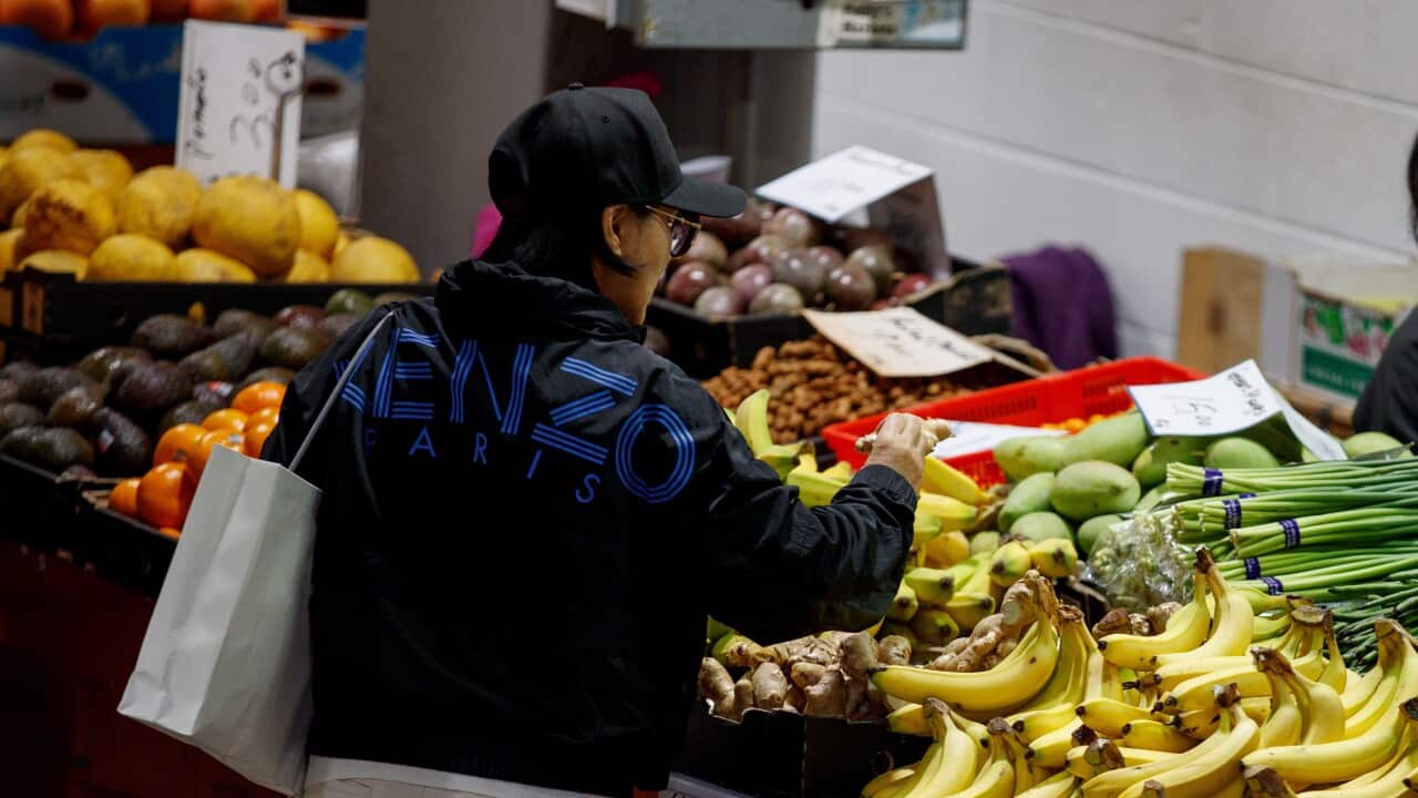 A woman reaches for bananas at a fruit and vegetable market.