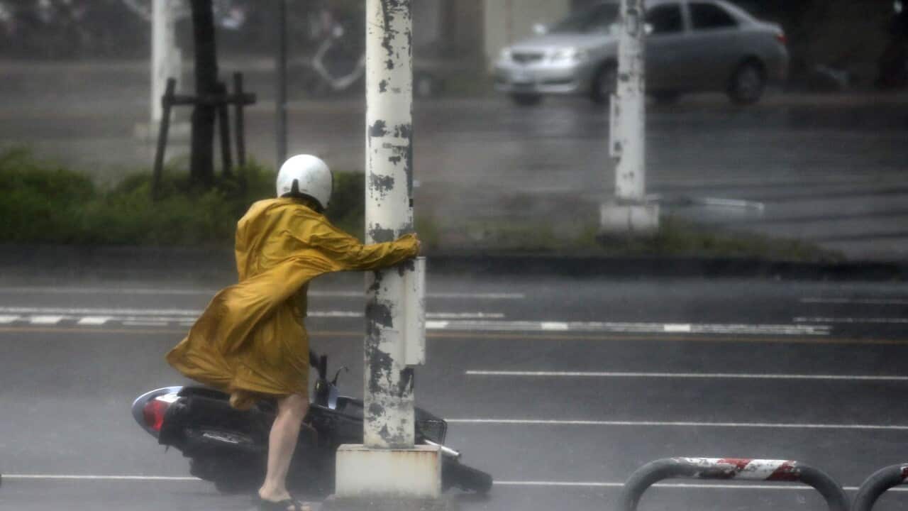 A motorist holds on to a post as she braves high winds and rain of Super Typhoon Meranti in Kaohsiung, southern Taiwan, 14 September 2016.