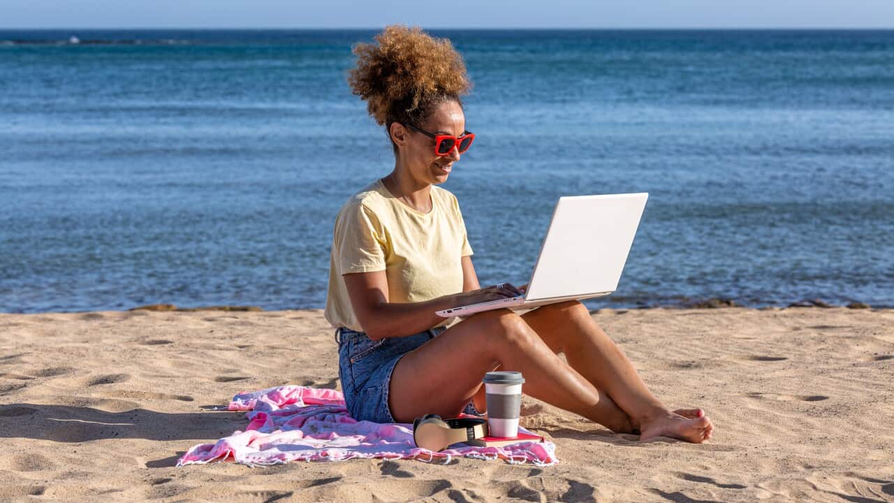 Hispanic woman browsing laptop on beach