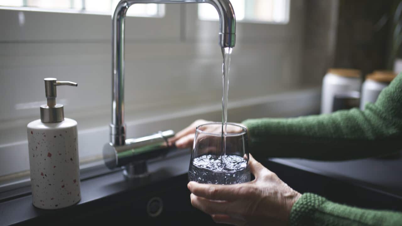 An image of a woman pouring a glass of water from a tap.
