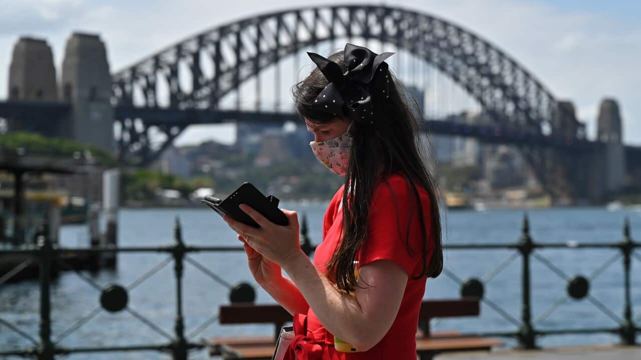 A person wears a mask while walking in front of the Sydney Harbour Bridge at Circular Quay in Sydney.