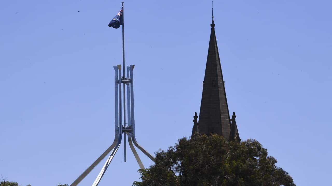 The tower of St Andrews Presbyterian Church is seen near the flag pole of the Australian Parliament House in Canberra, Tuesday, December 21, 2021. (AAP Image/Lukas Coch) NO ARCHIVING