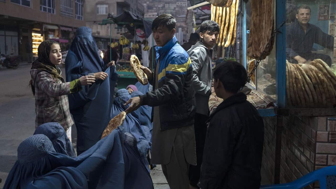A man distributes bread to Burka-wearing Afghan women outside a bakery in Kabul