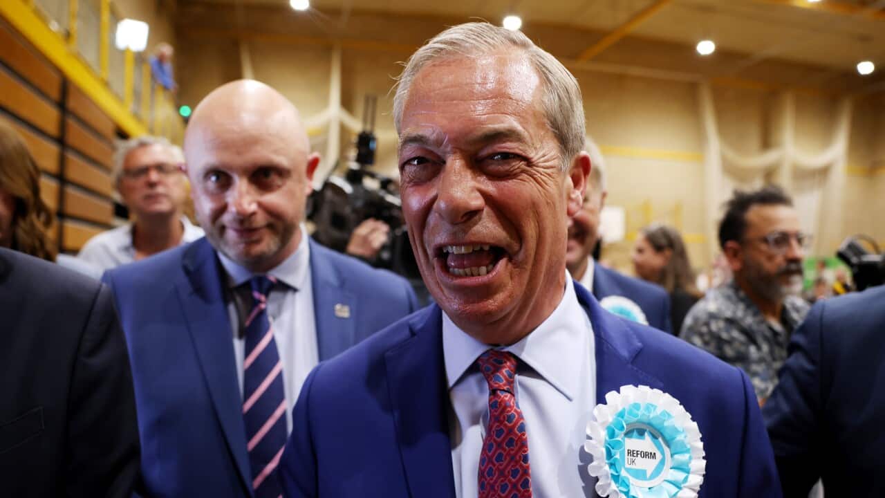 A man (Nigel Farage) with a blue suit and red and blue patterned tie wearing a Reform UK badge.