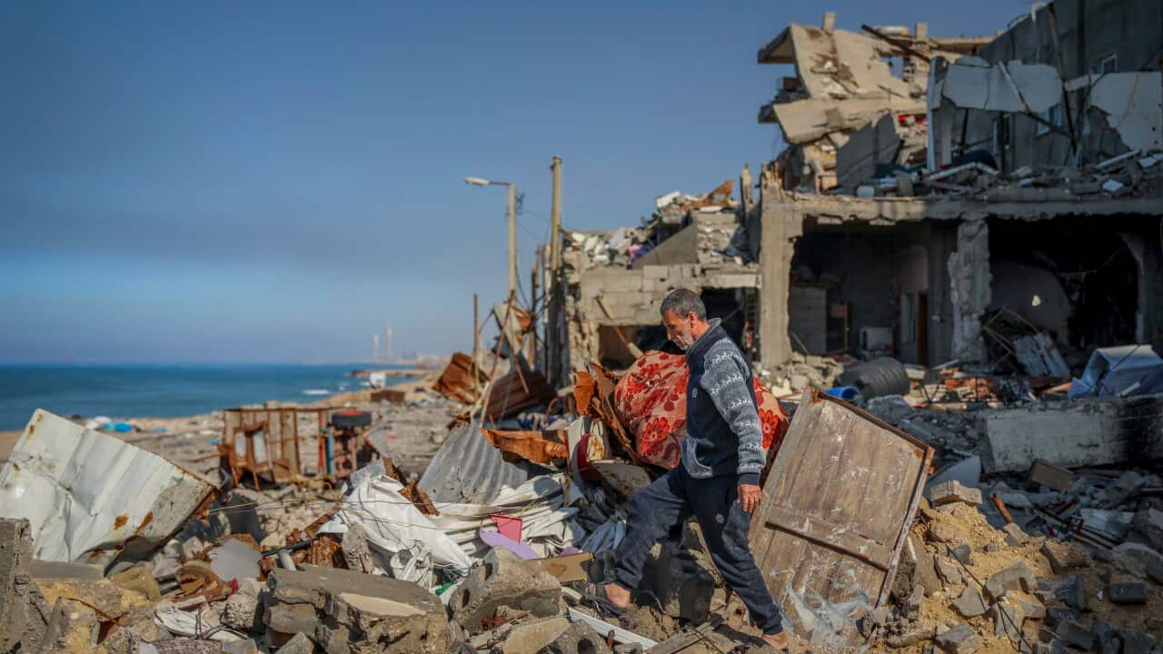A Palestinian man walks in the rubble of destroyed buildings in Gaza City, with the sea in the background