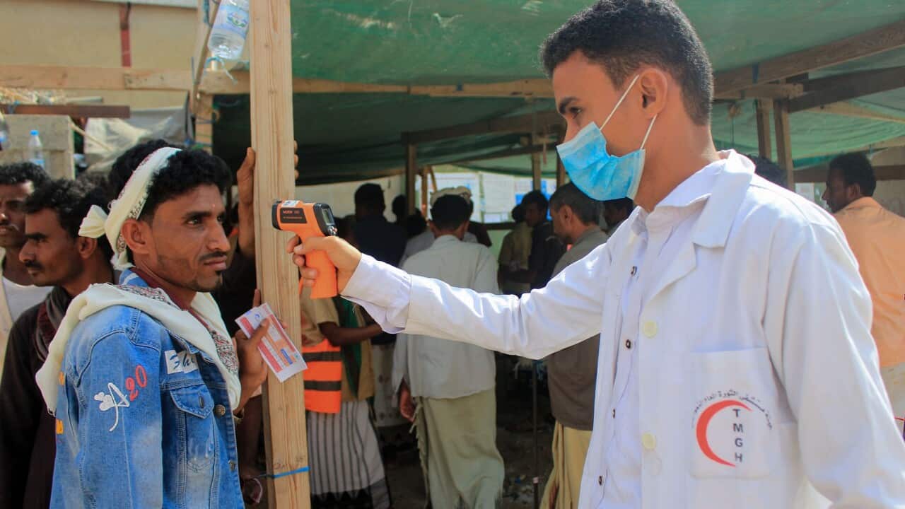A healthcare worker checks the temperature of displaced Yemenis amid the COVID-19 pandemic