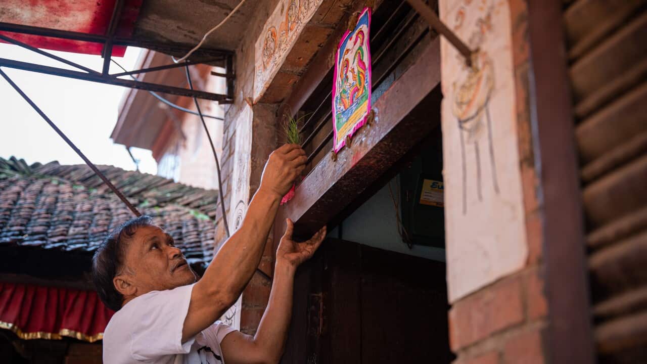 A man sticks a poster of the serpent deity (naga) above his doorstep during the Nag Panchami festival.