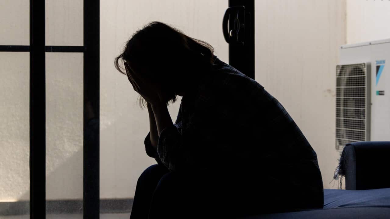 A grayscale image of a woman sitting on a couch with her head in her hands.