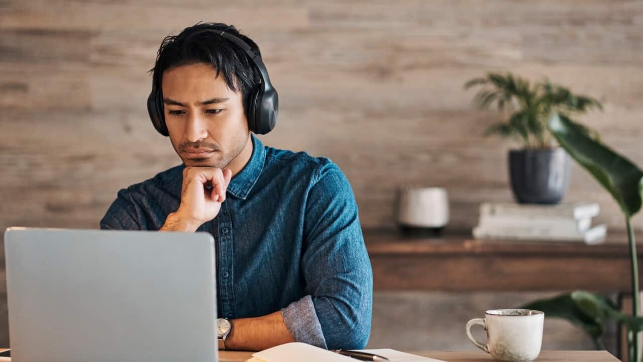 Businessman, headphones and laptop webinar in office with coffee on table, video call or watching video. Zoom call, video conference and male from Canada in online meeting with book and pen on desk.